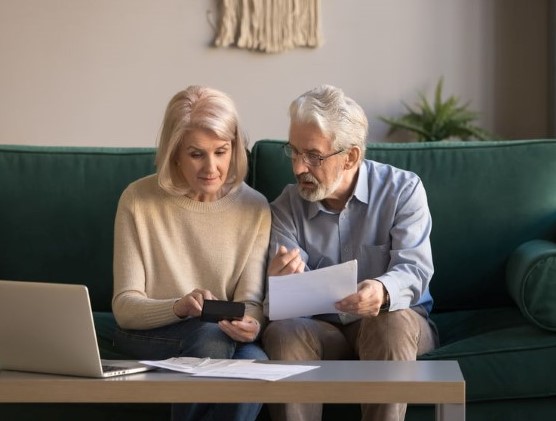 an elderly couple in their living room looking at paperwork and a phone