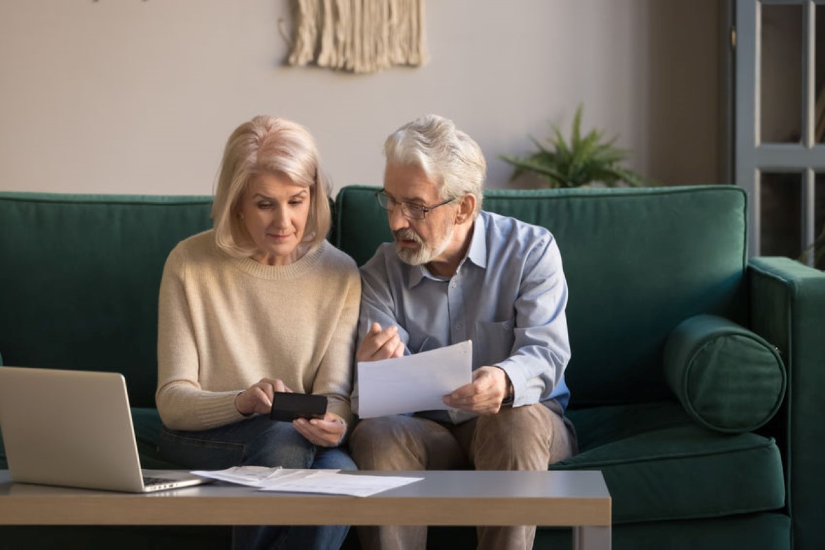 an elderly couple looking at a phone and papers in their living room