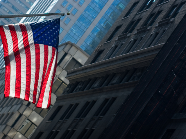 an American flag blowing in the wind with a high rise building in the background